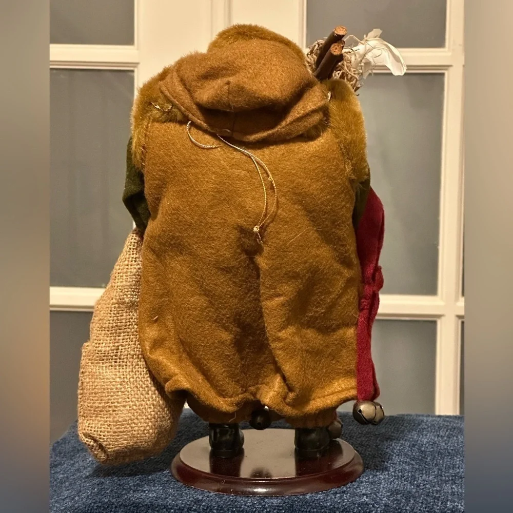 Shaggy haired and bearded Santa wears a brown cape and carries a burlap sack.